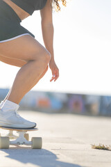 Young woman practices skateboarding on a sunny day near a colorful wall with graffiti © KONSTANTIN SHISHKIN