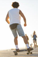 Skater rides through a sunny coastal path while other people walk nearby in the late afternoon © KONSTANTIN SHISHKIN