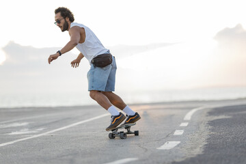 Skater rides down a coastal road while two friends walk in the background during sunset © KONSTANTIN SHISHKIN