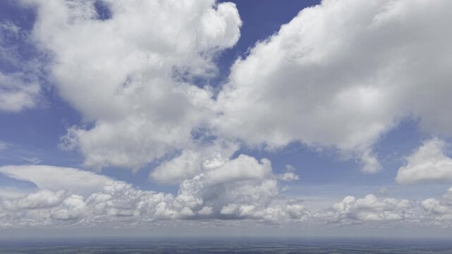 Towering cumulus cloud formations building over flat rural countryside, high aerial sky view
