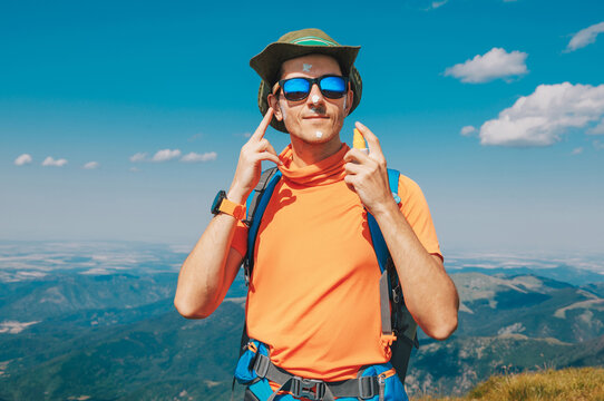 Hiker applying sunscreen to his face, ensuring skin protection during outdoor mountain adventure under a clear blue sky