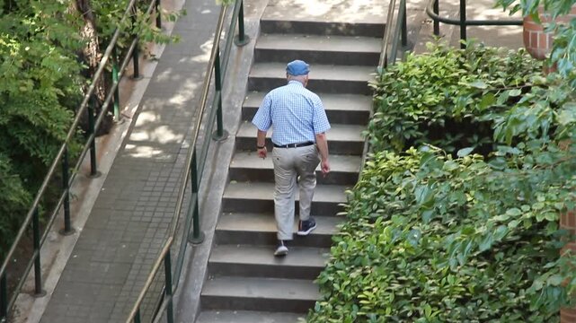 Viejo activo  subiendo escalones abuelo en escaleras calle con camisa corta, gorra, barandilla y matorral pasos y ejercicio tercera edad vejez y longevidad