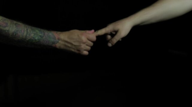 Black background, close-up of hands, one person pulling another's finger