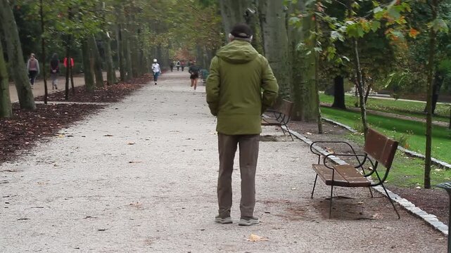 Viejo andando lento y mujer corriendo en parque persona mayor caminando y runner footing de frente con &aacute;rbol y banco
