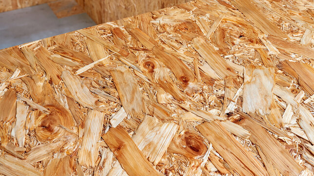 Extreme close up of OSB chipboard texture against a layered background of oriented strand board panels, irregular wood strands and pressed fibers clearly visible, natural beige and honey brown tones