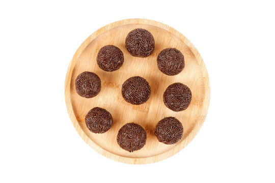 Traditional Brazilian chocolate brigadeiro coated in sprinkles, on a round bamboo tray, isolated on a white background.