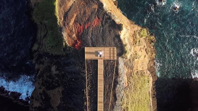 Rising drone unveils the full boardwalk leading to Farolim dos Fenais da Ajuda lighthouse, Sao Miguel, Azores