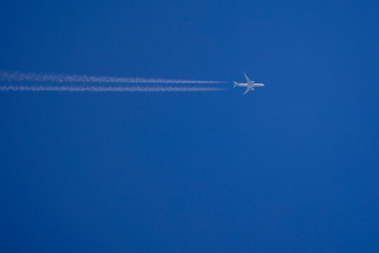 Passenger plane in clear blue sky flying horizontally to the right with a vapor trail behind