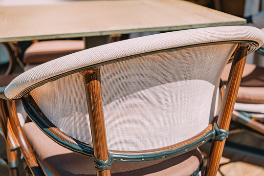 Rattan bistro chair at cafe table, close-up detail of woven backrest and wood frame, outdoor seating.