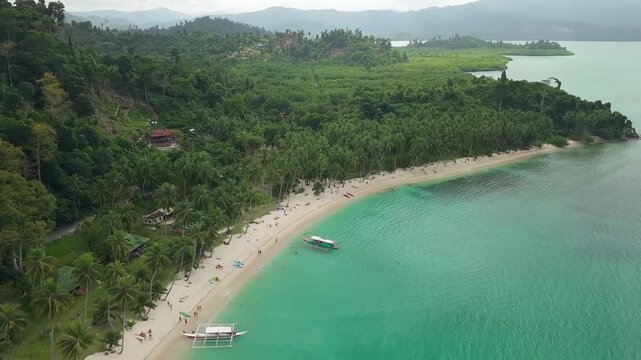 Aerial drone footage of White Beach in Port Barton, San Vicente, Palawan, Philippines. The video shows the long white sand beach, dense coconut palm forest and turquoise tropical waters 