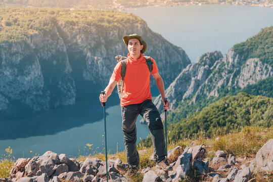 Young man standing on mountain top, looking at scenic nature view with deep canyon and river, enjoying trekking adventure