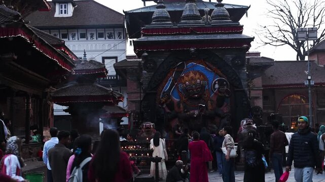 Worshippers gather before the towering stone Shree Kal Bhairav relief at evening, butter lamps at its base, Kathmandu, Nepal