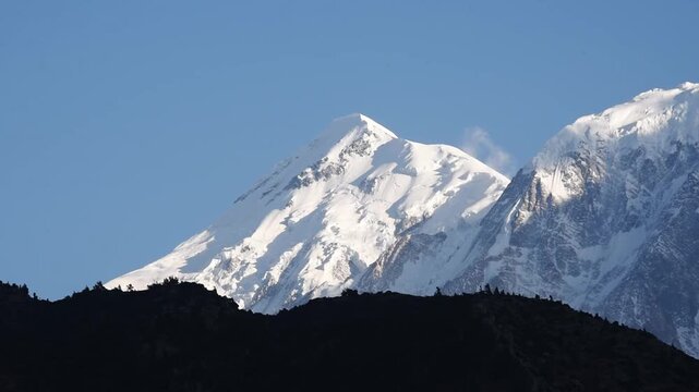 Broad glaciated summit of the Nilgiri massif rising above a dark ridge silhouette, Upper Mustang, Nepal