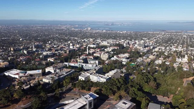 Aerial drone footage flying over the University of California, Berkeley campus, revealing the cityscape, San Francisco Bay, and the iconic Golden Gate Bridge in the hazy distance on a sunny day