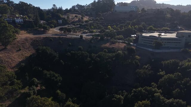 Aerial footage showcasing the University of California Berkeley campus nestled among the green, rolling hills under a bright, sunny sky, with buildings and winding roads visible