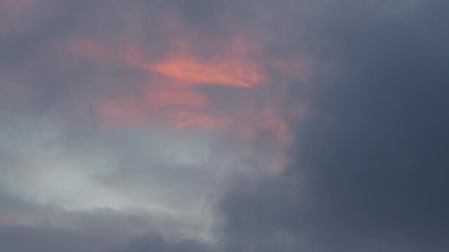 Bands of pink lit cloud drift above a darker grey layer as the light fades at the end of the day.
