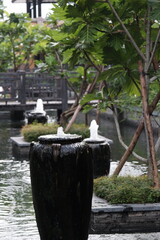 Fototapeta premium Water bubbling from traditional ceramic urn in outdoor reflection pool surrounded by green foliage