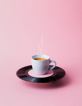 Steaming Coffee Cup on Vinyl Record Saucer over Pink Background