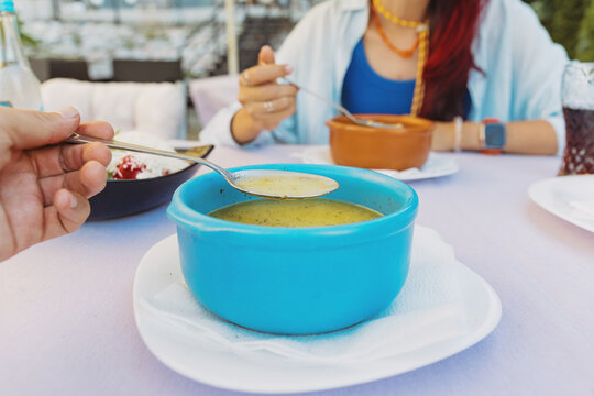 Woman smiling and looking away while enjoying a healthy bowl of soup at an outdoor cafe, dining al fresco