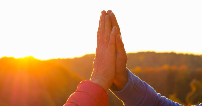 CLOSE UP, LENS FLARE, SILHOUETTE: Two adult people give each other high five as low sun shines between their hands. Natural moment of celebration, joy and human connection after autumn hike in nature.