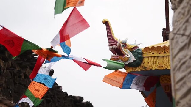 Carved dragon roof finial and Buddhist prayer flags against bright sky in Marpha