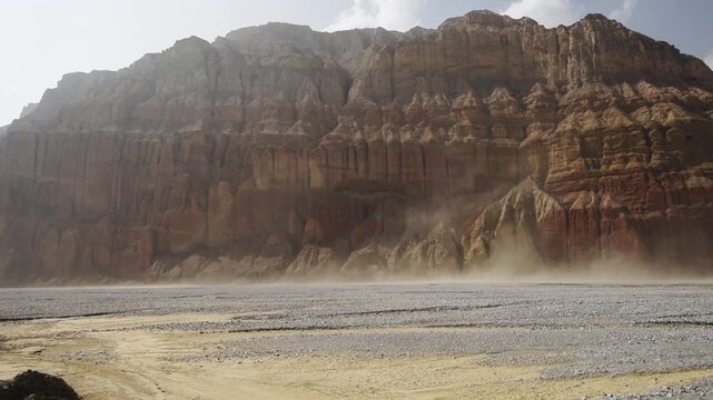 Wind-blown dust drifts past a red and ochre cliff wall in the Kali Gandaki valley, Upper Mustang