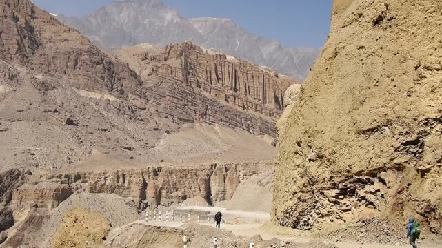 Trekkers on a dirt road below banded cliffs in the Kali Gandaki valley between Chele and Thangbe