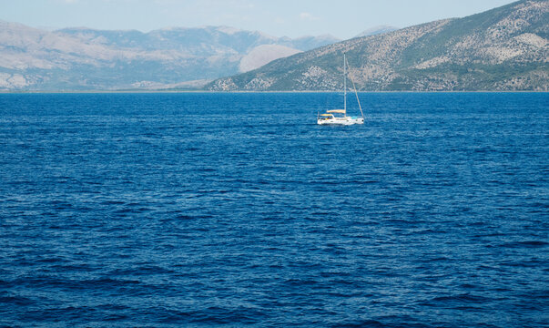 Monohull sailing yacht anchored in clear blue sea near the coast of Corfu island in Greece during a partly cloudy day, summer vacation concept