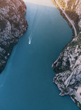 Boat navigating the Danube River through the Iron Gates gorge, surrounded by towering cliffs and a scenic road