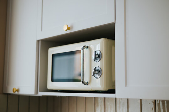 A microwave oven is placed inside kitchen cabinetry, showing its front panel and chrome handle. The oven is located beneath upper cabinets with golden knobs, creating a functional kitchen space