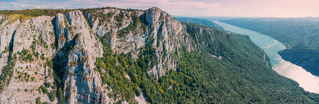 Panoramic aerial view of dramatic limestone cliffs framing a wide Danube river winding through Iron Gate gorge and valleys at sunset. Travel concept.
