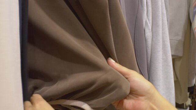 A detailed macro view shows a female hand with a clean white manicure sorting through a minimalist collection of beige, grey, and blue apparel on hangers. The video emphasizes a calm, aesthetically pl