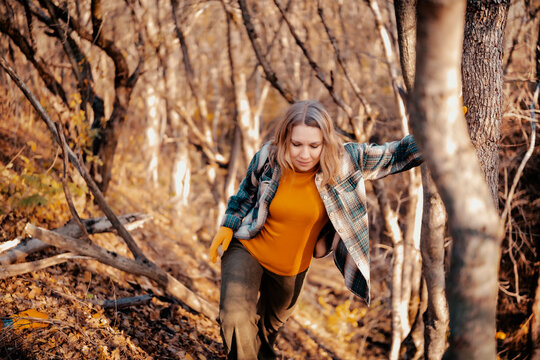 Energetic woman on autumn hike climbing up steep forest hill - outdoor survival. Active female traveler overcoming obstacles in nature woodland. Physical endurance and fitness concept.