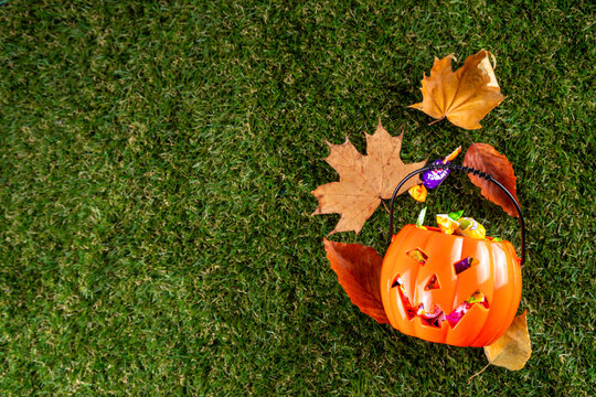 Trick or treat Halloween holiday outdoor party background. Various Halloween accessories, ghost decoration, basket with candies, colorful pumpkins, autumn fall leaves on green grass lawn background