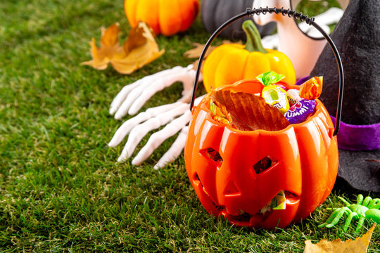 Trick or treat Halloween holiday outdoor party background. Various Halloween accessories, ghost decoration, basket with candies, colorful pumpkins, autumn fall leaves on green grass lawn background