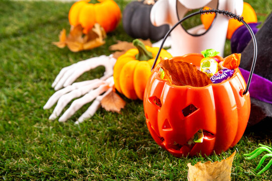Trick or treat Halloween holiday outdoor party background. Various Halloween accessories, ghost decoration, basket with candies, colorful pumpkins, autumn fall leaves on green grass lawn background