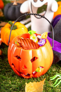 Trick or treat Halloween holiday outdoor party background. Various Halloween accessories, ghost decoration, basket with candies, colorful pumpkins, autumn fall leaves on green grass lawn background