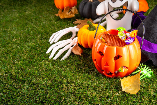 Trick or treat Halloween holiday outdoor party background. Various Halloween accessories, ghost decoration, basket with candies, colorful pumpkins, autumn fall leaves on green grass lawn background