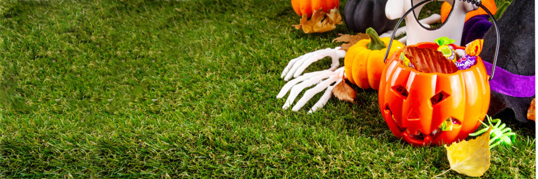 Trick or treat Halloween holiday outdoor party background. Various Halloween accessories, ghost decoration, basket with candies, colorful pumpkins, autumn fall leaves on green grass lawn background