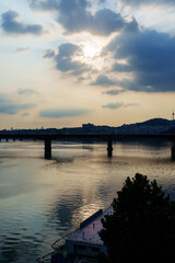 Obraz premium Sunset over river bridge and city skyline with cloudy sky