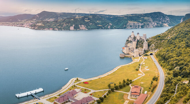 Sweeping autumn aerial of Golubac Fortress hugging the wide Danube, hills and wind turbines stretching to the horizon