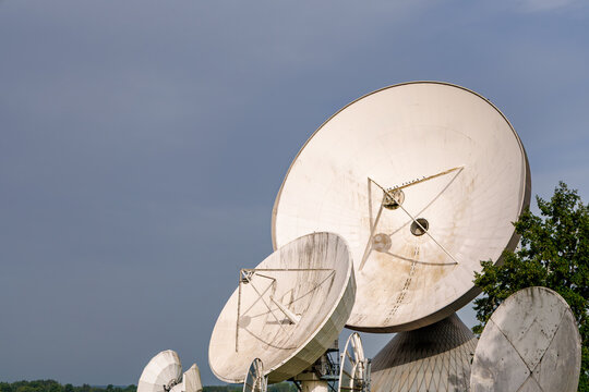 Group of large white parabolic satellite dish antennas pointed towards sky, telecommunication and space research technology concept
