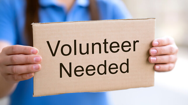 Volunteer holding cardboard sign with bold black text asking for help and community service support during local outreach program event