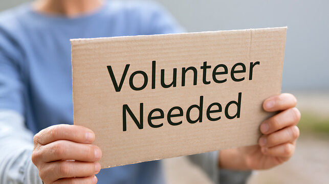 Person hold cardboard sign with text volunteer needed, close up shot showcasing community service hiring campaign for social work and charities