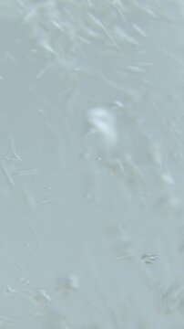 A stream of clear liquid pours into the clear water and gradually spreads out in a wavy brown pattern, swirling and spreading across the surface until it completely covers the calm water below.