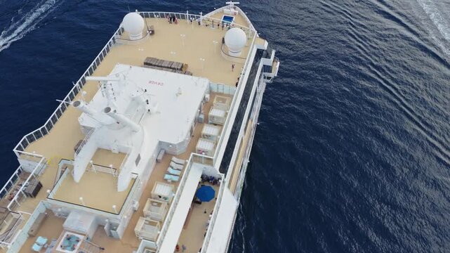 top down aerial view of the sun deck of a large cruise ship with a pool, hot tub and rows of sun loungers occupied by passengers at sea, montenegro