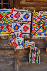 Obraz premium Traditional Bulgarian woven rugs and handmade textile bags. Colorful Bulgarian woven rugs and handmade textile bags displayed on rustic wooden wall. Authentic folk craft, vibrant ethnic ornament