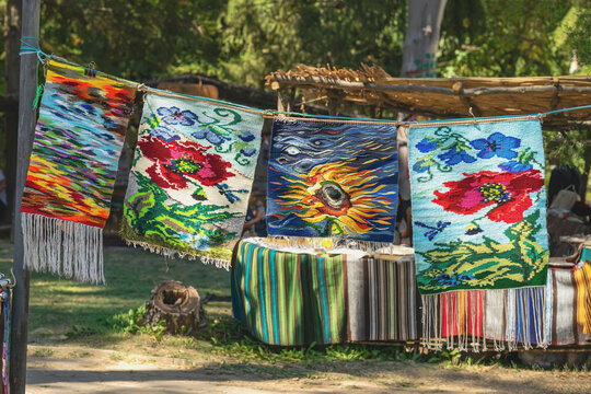 Colorful handmade carpets and woven rugs with floral and artistic patterns displayed outdoors at a traditional craft festival in Kotel, Bulgaria. Bulgarian textile heritage and folk craftsmanship