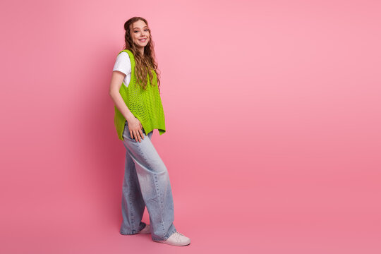 Young woman wearing a bright green vest stands against a pink background smiling in casual fashion