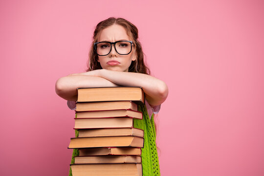 Young student girl with glasses leans on stack of book against pink background
